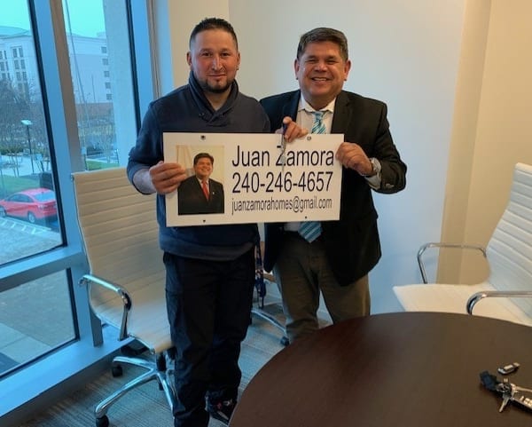 Proud clients holding the Juan Zamora Homes sign at closing